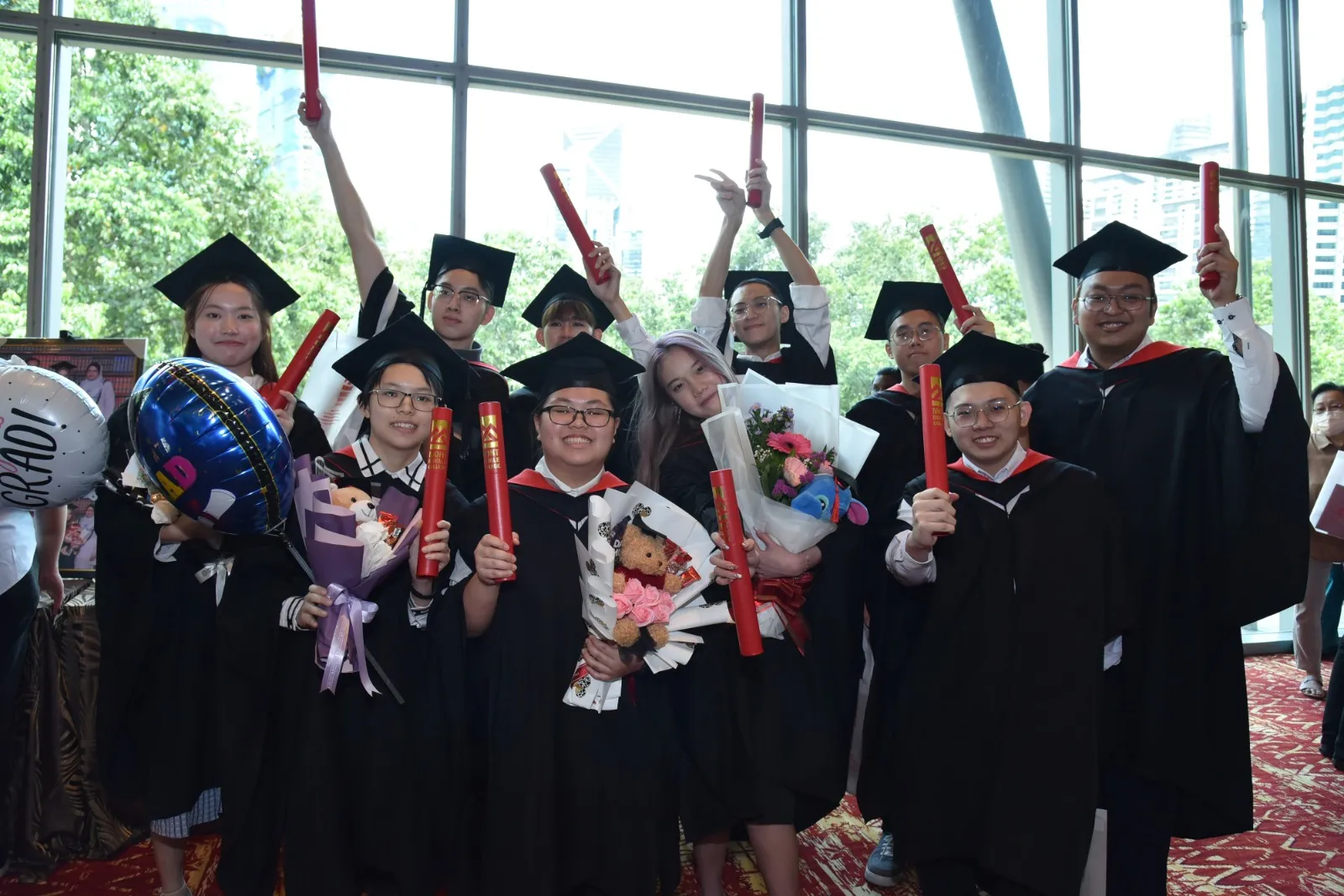 Mont Royale graduates in gowns and mortarboards raising their scrolls and bouquets at their graduation ceremony